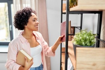 home improvement and people concept - happy smiling woman arranging books on shelving. smiling woman arranging books on shelving at home
