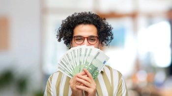 finance, currency and people concept - happy man holding euro money banknotes over office background. happy man with euro money at office