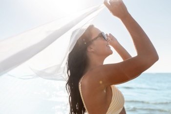 people, summer and swimwear concept - happy smiling young woman in bikini swimsuit with cover-up on beach. woman in bikini swimsuit with cover-up on beach