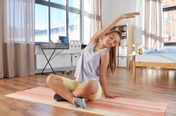 sport, fitness and healthy lifestyle concept - smiling teenage girl exercising on yoga mat and stretching spine at home. happy teenage girl exercising on yoga mat at home