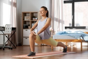 sport, fitness and healthy lifestyle concept - smiling teenage girl exercising on yoga mat and stretching leg at home. happy teenage girl exercising on yoga mat at home