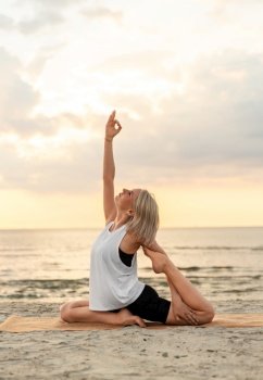 fitness, sport, and healthy lifestyle concept - woman doing yoga mermaid pose on beach over sunset. woman doing yoga mermaid pose on beach