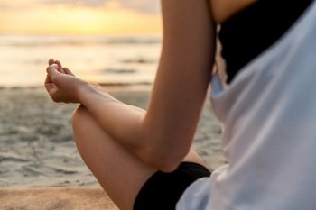 yoga, mindfulness and meditation concept - close up of woman meditating in lotus pose on beach over sunset. woman meditating in lotus pose on beach