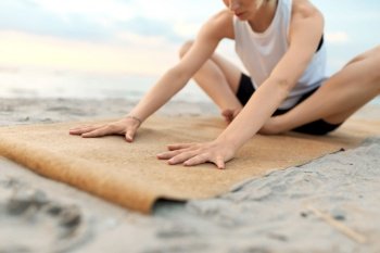 fitness, sport, and healthy lifestyle concept - close up of woman doing yoga stretching pose on beach over sunset. woman doing yoga stretching pose on beach