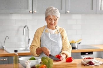 healthy eating, food cooking and culinary concept - happy smiling senior woman with knife chopping red pepper on kitchen at home. happy woman chopping red pepper on kitchen