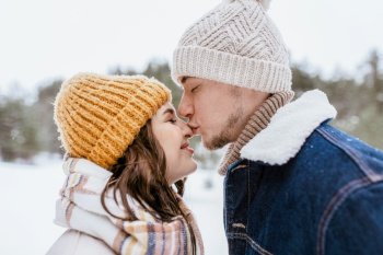 people, love and leisure concept - happy man kissing woman’s nose in winter forest. happy man kissing woman’s nose in winter