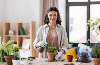 people, gardening and housework concept - happy woman in gloves with spray planting pot flowers at home. happy woman planting pot flowers at home