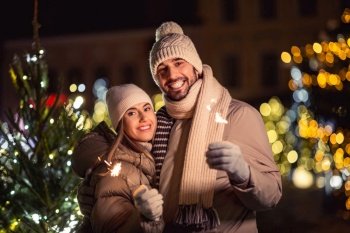 winter holidays and people concept - happy smiling couple with sparklers over christmas lights in evening. happy couple with sparklers over christmas lights