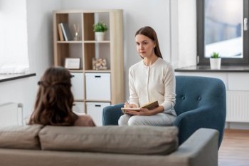 psychology, mental health and people concept - psychologist with notebook and woman patient at psychotherapy session. psychologist and woman at psychotherapy session