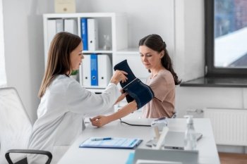 medicine, healthcare and people concept - female doctor with tonometer measuring woman patient’s blood pressure at hospital. female doctor with tonometer and patient at clinic