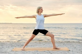 fitness, sport, and healthy lifestyle concept - happy woman doing yoga warrior pose on beach over sunset. happy woman doing yoga warrior pose on beach