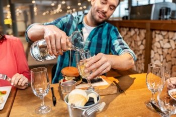 food, leisure and people concept - happy smiling man having dinner at restaurant and pouring water from jug to glass. happy smiling pouring water to glass at restaurant