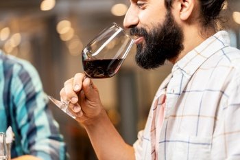 leisure, drinks and people concept - close up of happy man with glass drinking red wine at restaurant. man with glass drinking red wine at restaurant