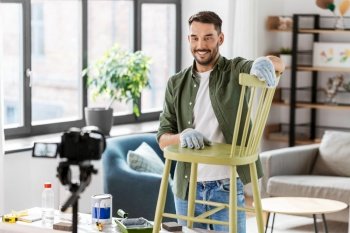 blogging, furniture restoration and home improvement concept - happy smiling man or blogger with camera showing old wooden chair renovation and recording tutorial video. man or blogger showing old chair renovation
