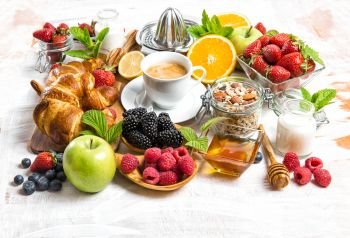 Breakfast with coffee, croissants, muesli, milk, fresh berries, fruits orange, apple. Healthy food concept