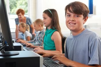 Portrait Of Male Elementary Pupil In Computer Class With Teacher