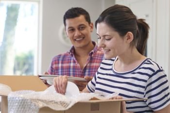 Young Couple Unpacking Boxes In Kitchen On Moving Day