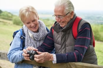 Senior Couple Hiking In Countryside Standing By Gate And Taking Photo With Camera    