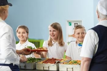 Pupils In School Cafeteria Being Served Lunch By Dinner Ladies