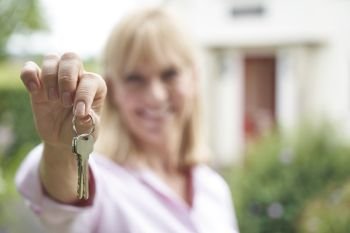 Portrait Of Mature Woman Standing In Garden In Front Of Dream Home In Countryside Holding Keys                             