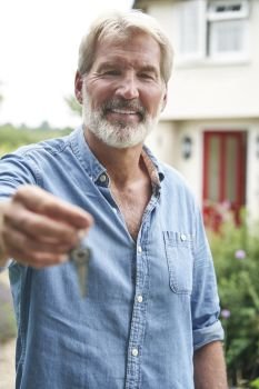 Portrait Of Mature Man Standing In Garden In Front Of Dream Home In Countryside Holding Keys