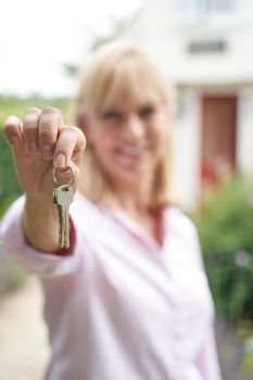 Portrait Of Mature Woman Standing In Garden In Front Of Dream Home In Countryside Holding Keys         