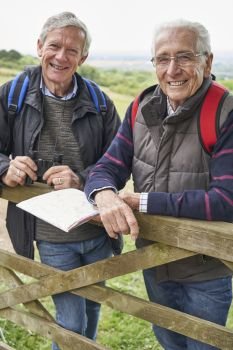 Portrait Of Two Retired Male Friends On Walking Holiday Resting On Gate With Map                                  