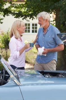 Mature Woman Bringing Hot Drink To Man Restoring Classic Sports Car Working On Engine Under Hood