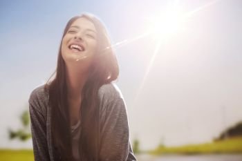 Close up portrait of a smiling teenage girl standing outdoors with her eyes closed with sun in the background