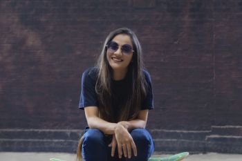 Beautiful young woman sitting on skateboard on Street Wearing Sunglasses