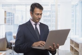 Businessman using a laptop holding in hand while standing in office