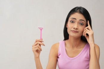 A young woman thinking whether to use hair removal razor.