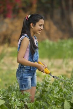 Young girl trimming plants in garden using a hedge shear or gardening scissors.