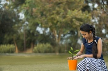 Young girl planting a sapling in a small flower pot sitting in a park.