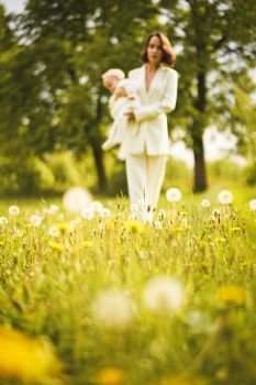 Outdoor fashion portrait of young beautiful mother and little cute daughter on a meadow with dandelions. Spring image