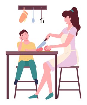 Young mother cooking with her son at kitchen, people sitting near kitchen table. Woman cutting vegetables tomato with knife. Happy family spend leisure time together. Relationships of parents and kids. Young mother cooking with her son, cutting tomato at kitchen, people sitting near kitchen table