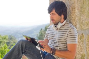 young man working with a tablet pc listening music with headphones, outdoor