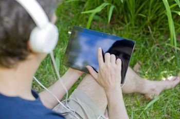 detail of young man relaxing with a tablet pc listening music with headphones on a the park, outdoor