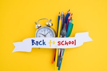 back to school concept - alarm clock and school supplies with back to school text on ribbon. back to school