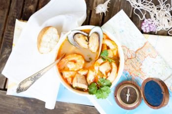 Plate of Bouillabaisse french seafood soup with compass and mediterranean sea maps, top view. Bouillabaisse french seafood soup