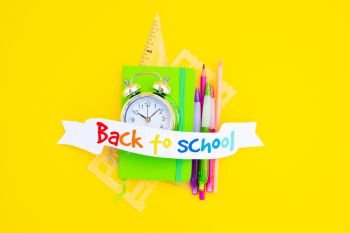 back to school concept - small alarm clock and school supplies on bright yellow background. back to school