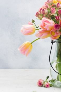 fresh pink and yellow tulips and roses flowers in glass vase close up on gray background. Pink and yellow tulips and roses