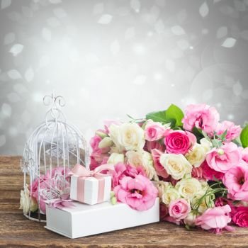bunch of pink and white fresh roses and eustoma flowers  with present  boxes and birdcage on wooden table . pink and white flowers