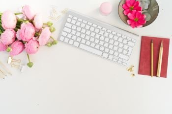 Flat lay home office workspace - modern keyboard with fresh ranunculus flowers, copy space on white background. Top view home office workspace