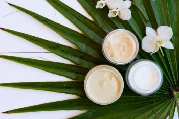 Coconut oil and cosmetics with green palm leaves top view, close up on white wooden background. Coconut oil nd cosmetics