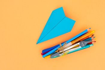 Back to school styled school supplies and blue paper plane on orange background with copy space. back to school