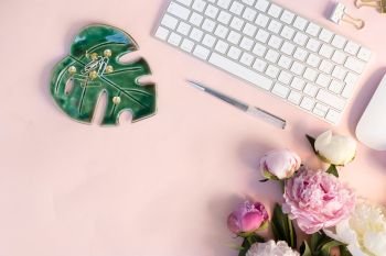 Flat lay home office workspace - modern white keyboard with and peony flowers, copy space on pink background. Top view home office workspace