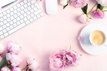 Flat lay home office workspace frame - modern keyboard with female accessories and fresh peony flowers, copy space on pink background. Top view home office workspace