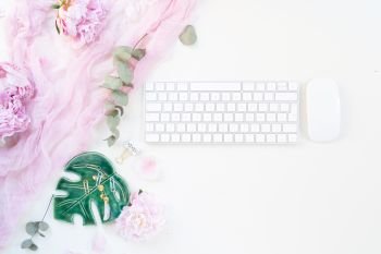 Flat lay home office workspace - modern keyboard with female accessories and fresh peony flowers. Top view home office workspace