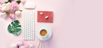 Flat lay home office workspace - modern keyboard with cup of coffee, office supplies and peony flowers, copy space on pink background banner. Top view home office workspace